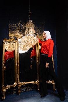 Fashion muslim model is posing near big expensive chandelier. Islamic religion. Girl near mirrors