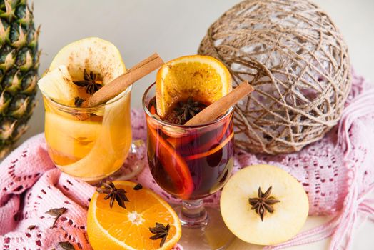 Mulled wine, grog and punch hot alcohol drinks on the table with seasonal decoration: pineapple, cinnamon, apple, orange, star anise. Seasonal spiced drink.