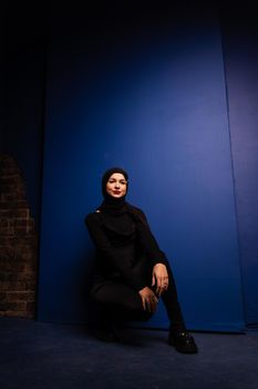 Fashion muslim model in black hijab is posing on blue background in studio. Islam religion