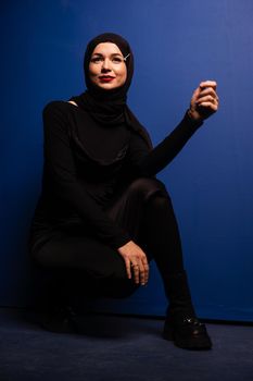 Fashion muslim model in black hijab is posing on blue background in studio. Islam religion