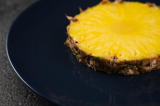 Piece of pineapple on blue plate close-up. Slice of yellow tropical fruit.