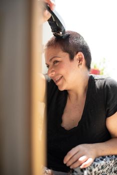 Happy young woman shaving your hair head with a razor machine and smiling at home, vertical high quality photo