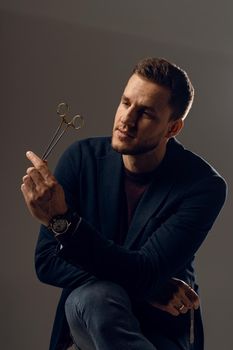 Doctor with surgical equipment needle and scissors. Handsome man weared casual business suit. Portrait of surgeon in studio