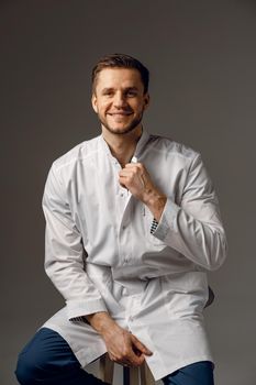 Surgeon weared in medical robe smile on dark background. Handsome happy doctor posing in studio