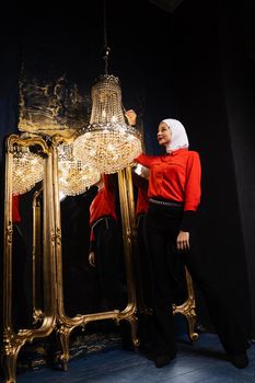 Fashion muslim model is posing near big expensive chandelier. Islamic religion. Girl near mirrors