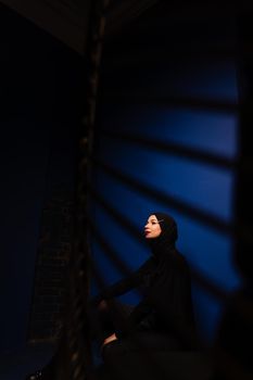 Fashion muslim model in black hijab is posing on blue background in studio. Islam religion creative photo.