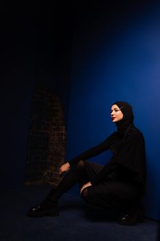 Fashion muslim model in black hijab is posing on blue background in studio. Islam religion creative photo.