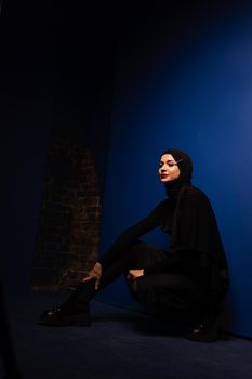 Fashion muslim model in black hijab is posing on blue background in studio. Islam religion creative photo.