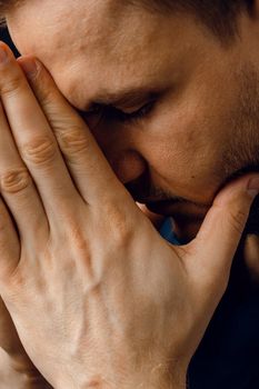 Close-up handsome man pray and believe in God. Orthodox Christian faith. Man cover his face with his hands and thinks about life