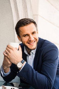 Man like coffee. Handsome man with cup of coffee in cafe. Morning lifestyle of male. Man is sitting on the summer terrace in cafe, drinking coffee and smiling