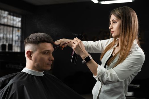 Woman barber making hairstyle in barbershop using clipper. Hairdresser cutting hair of handsome man