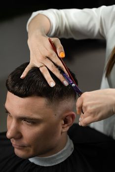 Haircut and styling in barbershop for handsome man. Woman making hairstyle using scissors