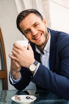 Man like coffee. Handsome man with cup of coffee in cafe. Morning lifestyle of male. Man is sitting on the summer terrace in cafe, drinking coffee and smiling