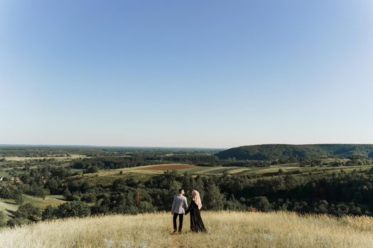 Muslim love story. Mixed couple smiles and hugs on the green hills . Woman weared in hijab looks to her man. Advert for on-line dating agency