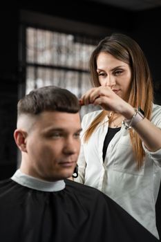 Woman barber making hairstyle in barbershop using clipper. Hairdresser cutting hair of handsome man