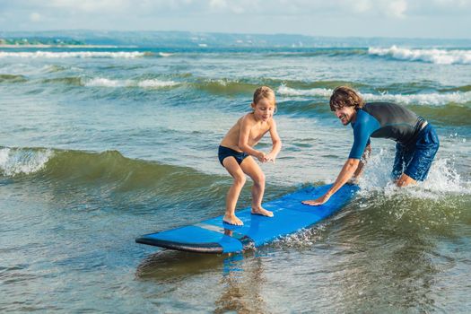 Father or instructor teaching his 4 year old son how to surf in the sea on vacation or holiday. Travel and sports with children concept. Surfing lesson for kids.