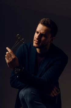 Doctor with surgical equipment needle and scissors. Handsome man weared casual business suit. Portrait of surgeon in studio