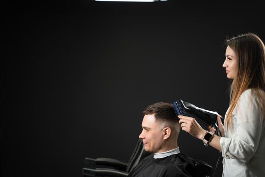 Drying hair after cutting in barbershop for handsome man. Woman hairdresser making hair style