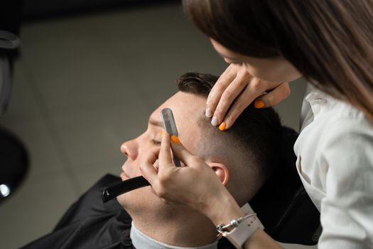 Straight razor cut man hair in barbershop. Attractive woman barber making hairstyle for handsome man