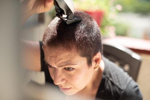 worried young woman shaving your hair head with a razor machine and smiling at home, horizontal high quality photo