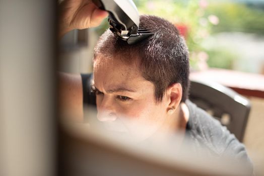 worried young woman shaving your hair head with a razor machine and smiling at home, horizontal high quality photo