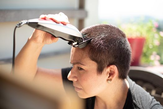 worried young woman shaving your hair head with a razor machine and smiling at home, horizontal high quality photo