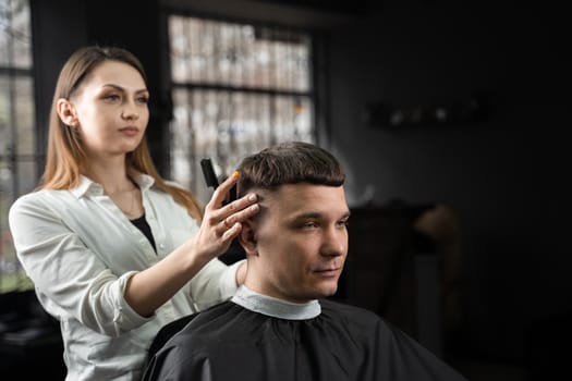 Woman barber making hairstyle in barbershop using clipper. Hairdresser cutting hair of handsome man