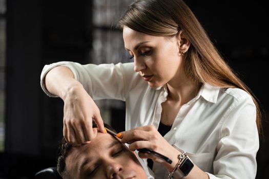 Straight razor cut man hair in barbershop. Attractive woman barber making hairstyle for handsome man