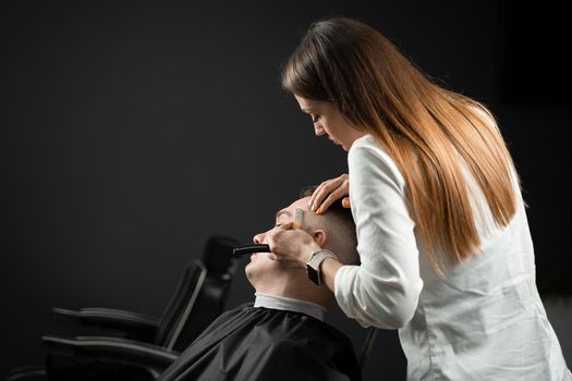 Straight razor cut man hair in barbershop. Attractive woman barber making hairstyle for handsome man