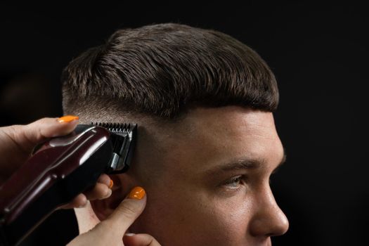 Woman barber making hairstyle in barbershop using clipper. Hairdresser cutting hair of handsome man