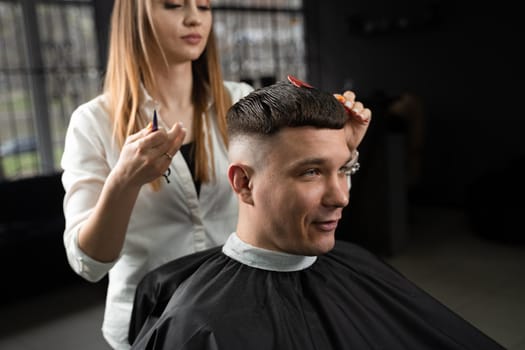 Woman barber making hairstyle in barbershop using clipper. Hairdresser cutting hair of handsome man