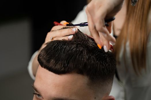 Haircut and styling in barbershop for handsome man. Woman making hairstyle using scissors