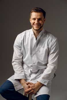 Surgeon weared in medical robe smile on dark background. Handsome happy doctor posing in studio