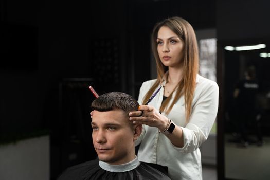 Haircut and styling in barbershop for handsome man. Woman making hairstyle using scissors