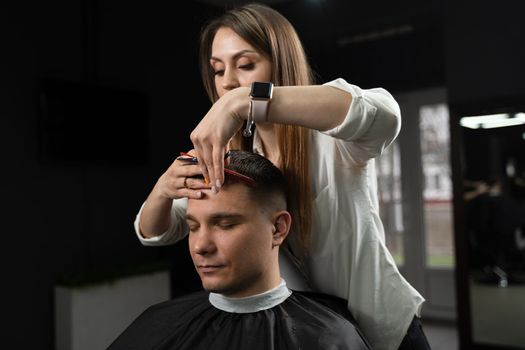 Haircut and styling in barbershop for handsome man. Woman making hairstyle using scissors