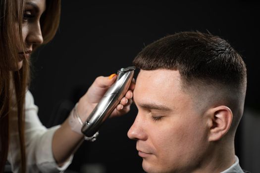 Trimming bangs of handsome man in barbershop. Woman hairdresser making hair style