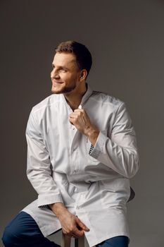 Surgeon weared in medical robe smile on dark background. Handsome happy doctor posing in studio