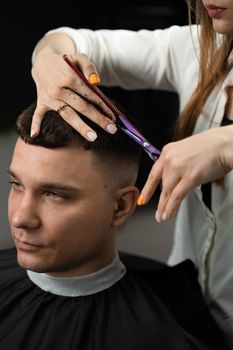 Haircut and styling in barbershop for handsome man. Woman making hairstyle using scissors