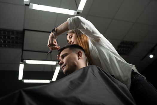 Haircut and styling in barbershop for handsome man. Woman making hairstyle using scissors