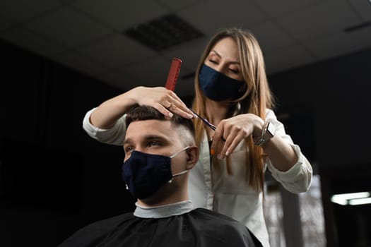 Barbershop service at coronavirus covid-19 period. Woman barber making hair for handsome man. Using mask