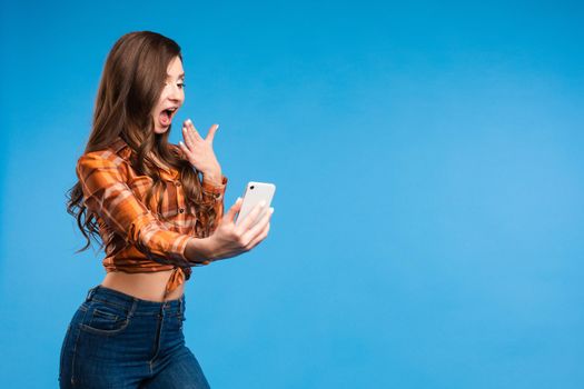 Full length portrait of happy stylish woman with charming smile in fashion sweater and brown skirt. She is standing and taking selfie with smartphone. Isolated on gray background