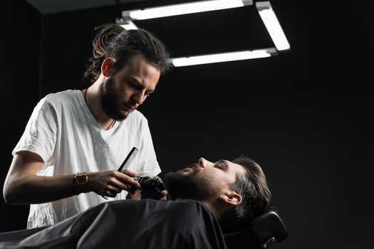 Handsome bearded man has hair and beard cut in barbershop. Dreadlock barber cuts client's hair.