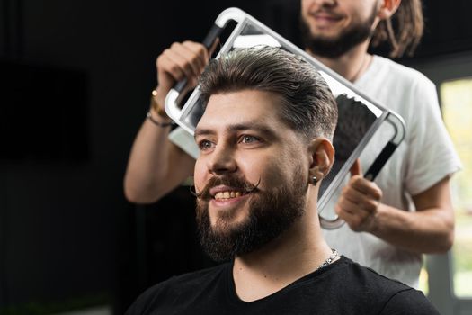 Happy and surprised bearded man looking in mirror in barbershop. Showing result of low fade machine hair.