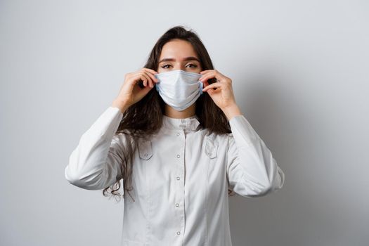 Doctor wearing medical mask on white background. Young attractive woman in medical robe. Quarantine coronavirus covid-19 trends.