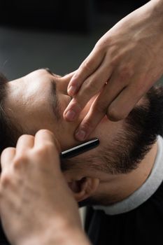 Straight razor cut mans beard in barbershop. Barber man making hairstyle for handsome man