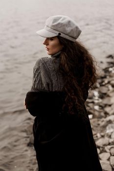 Girl with curly hair on the background of birch with stones and lake in autumn.