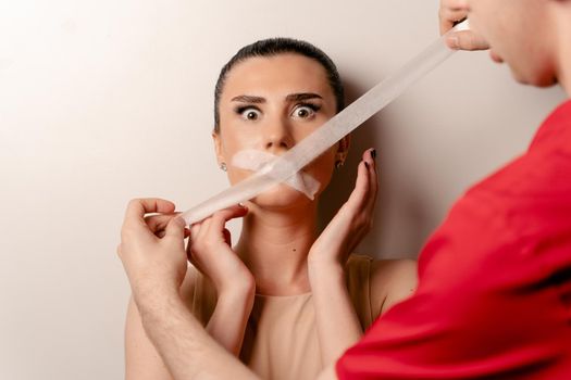 Model with glued mouth. Man covers woman mouth with tape. Stop talking