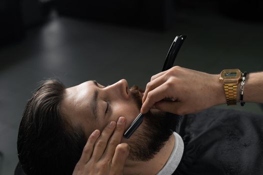 Straight razor cut mans beard in barbershop. Barber man making hairstyle for handsome man