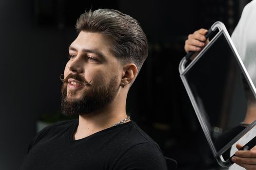 Barber with dreadlocks showing result of low fade machine hair and beard cut for bearded man in barbershop. Hairstyle with a smooth transition