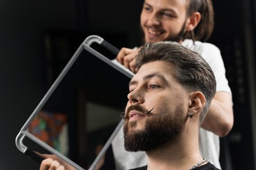 Barber with dreadlocks showing result of low fade machine hair and beard cut for bearded man in barbershop. Hairstyle with a smooth transition